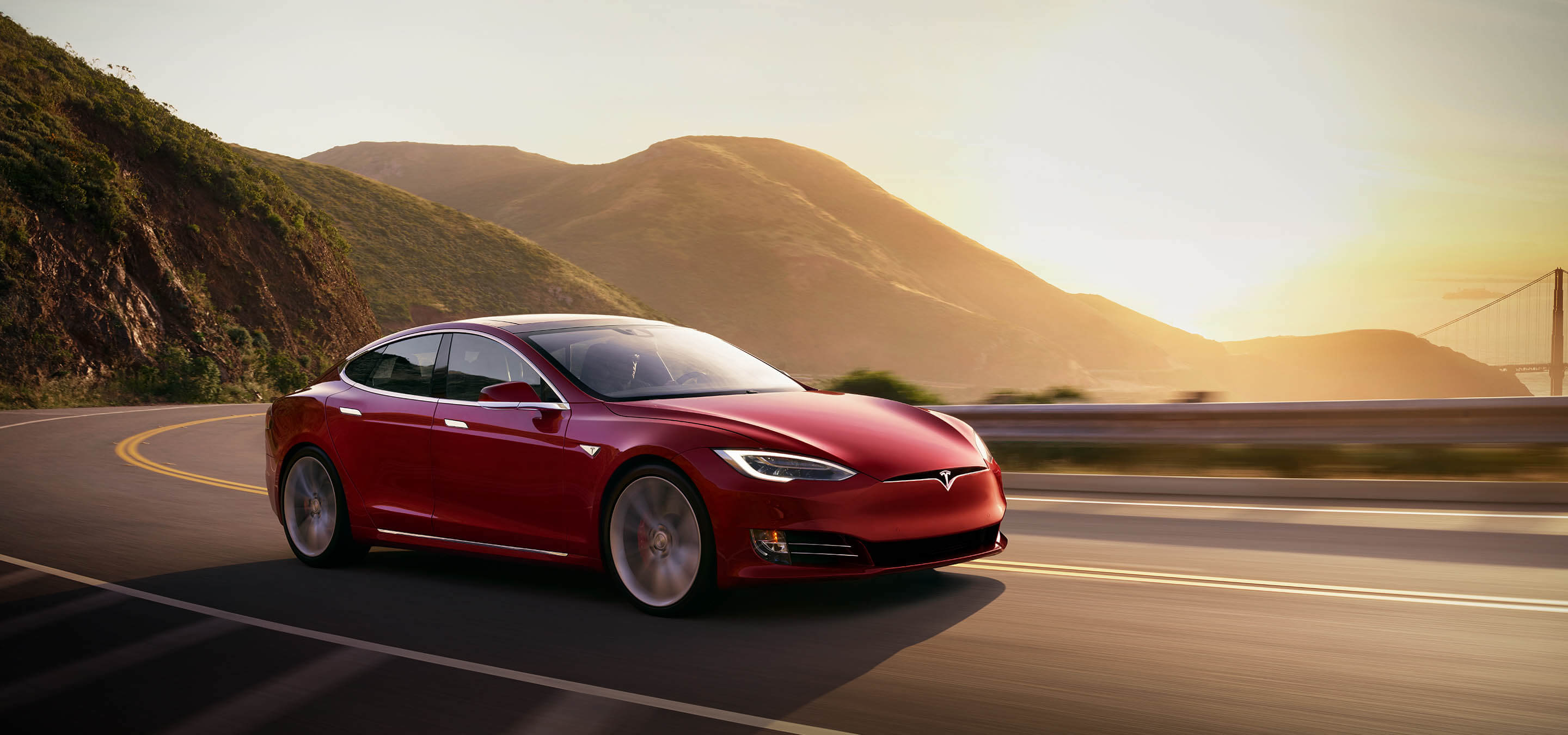 Tesla Model S en rouge conduisant sur les côtes de montagnes pendant une journée ensoleillée